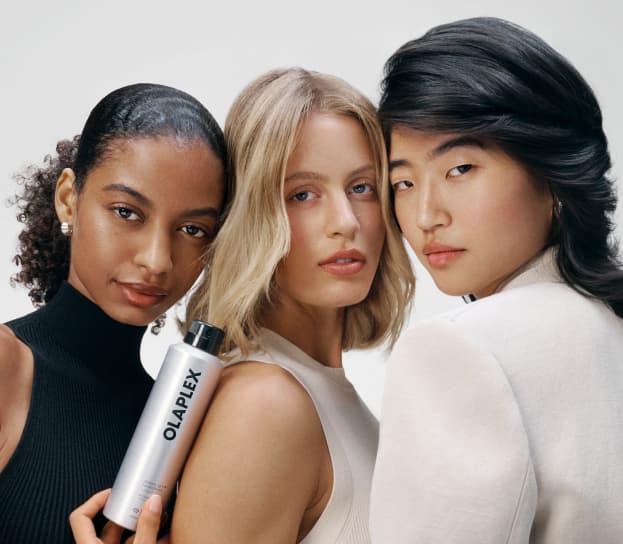 Three Glamsquad models with freshly styled hair, one holding a bottle of OLAPLEX styling spray, a Glamsquad styling partner product