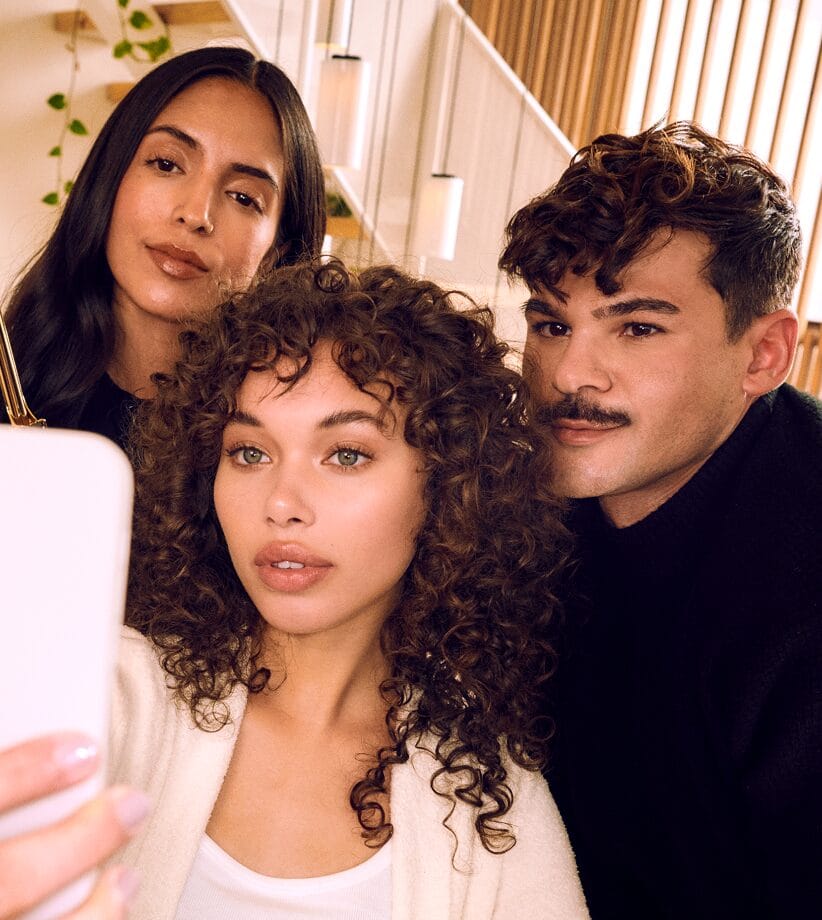 Three Glamsquad clients with fresh makeup and curly styled hair taking a selfie together indoors