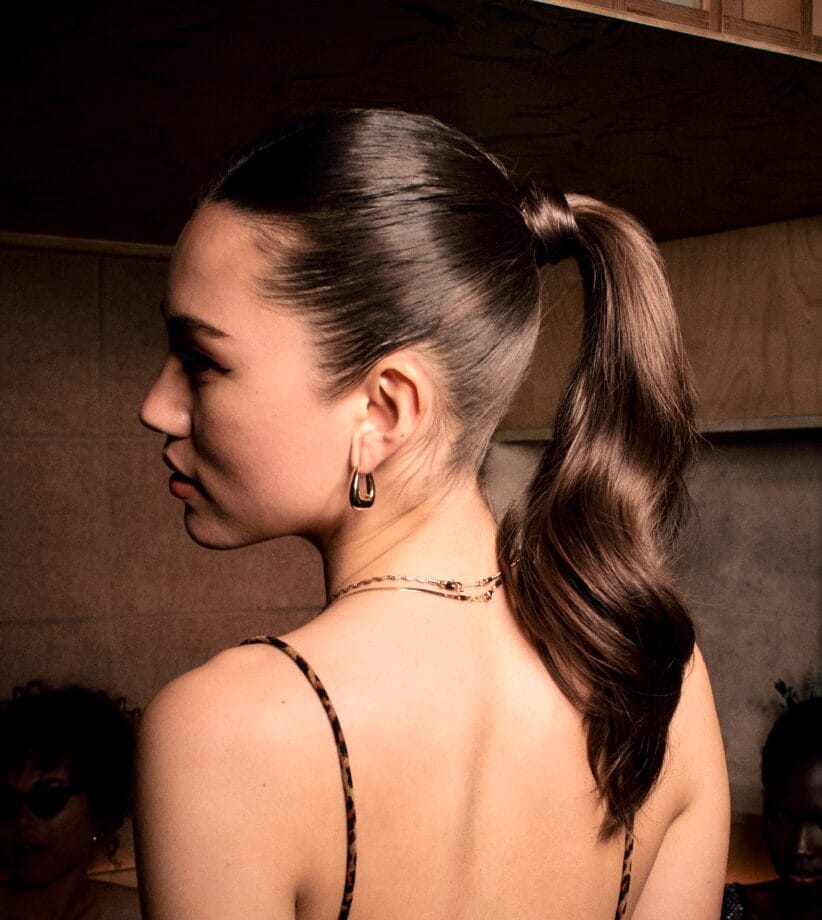Glamsquad client photographed from behind showing a sleek wavy high ponytail with gold hoop earrings