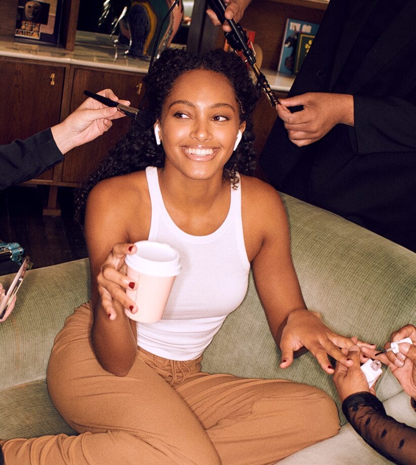 Smiling Glamsquad client relaxing with coffee while pros style her hair and paint her nails at home